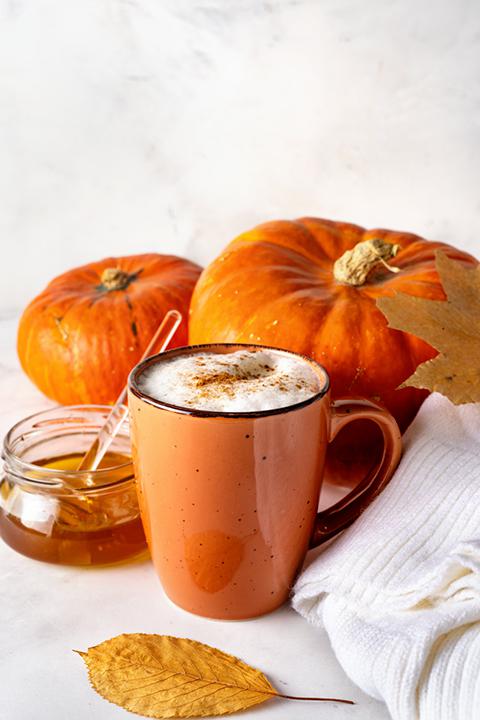 this warm PSL is surrounded by fall colored leaves, a warm white sweater, and a jar of honey to your taste