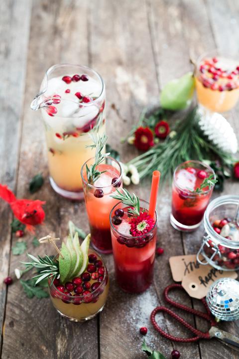 Wooden table with assortment of red and yellow beverages in glass cups with cranberry garnishes