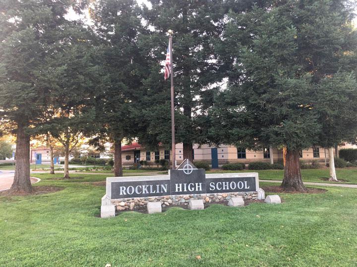 Rocklin High school sign with United States flag on green lawn with pine trees