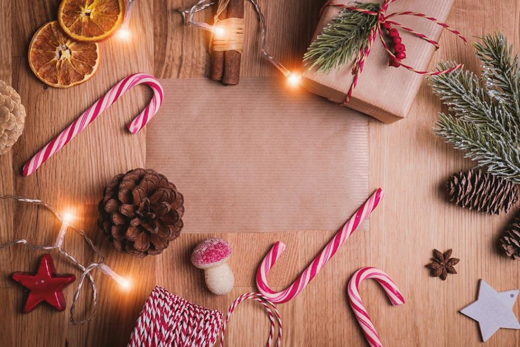 light brown wooden surface with dried orange slices red and white candy canes pinecones pine needles string brown wrapping paper and other crafting materials