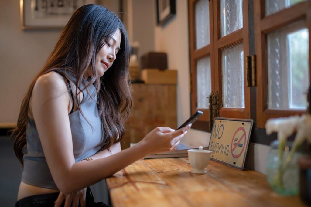 woman sitting at her desk looking at her phone and drinking a latte