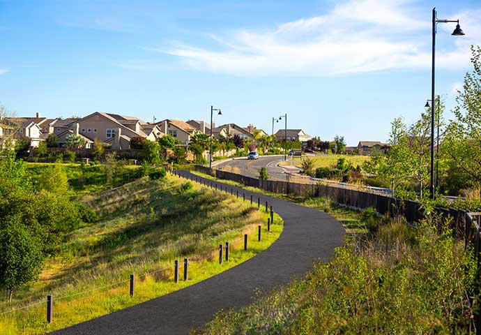 a gravel road overlooked by large houses, greenery, and an almost-cloudless blue sky