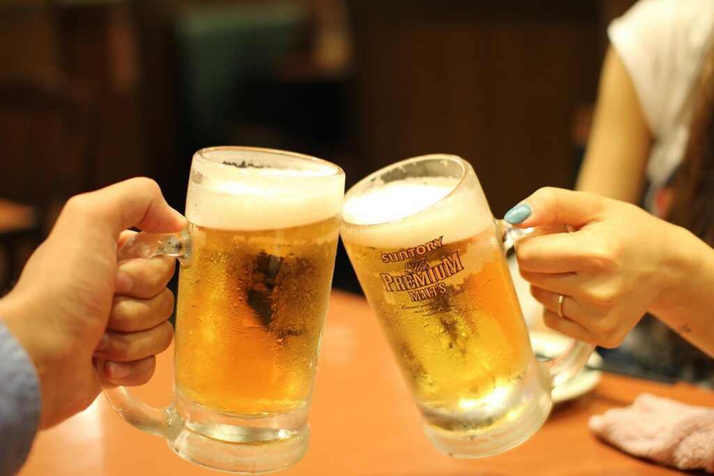 two people clinking mugs of beer labeled with “Suntory: The Premium Malts”
