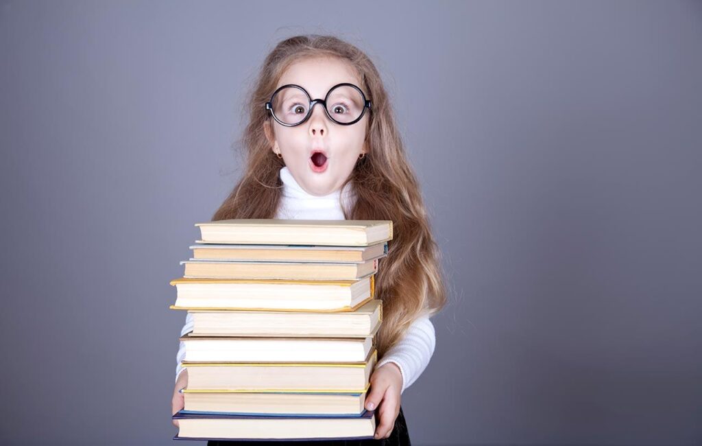 Excited little girl in glasses holds a stack of books