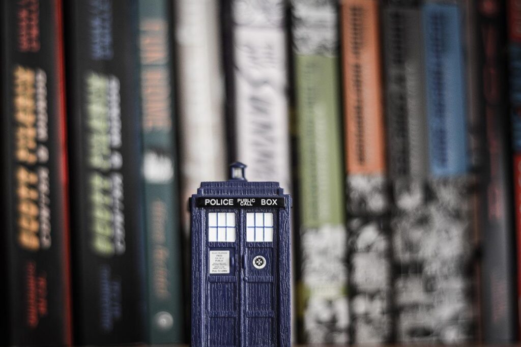 a mini TARDIS sits in front a blurred background of books