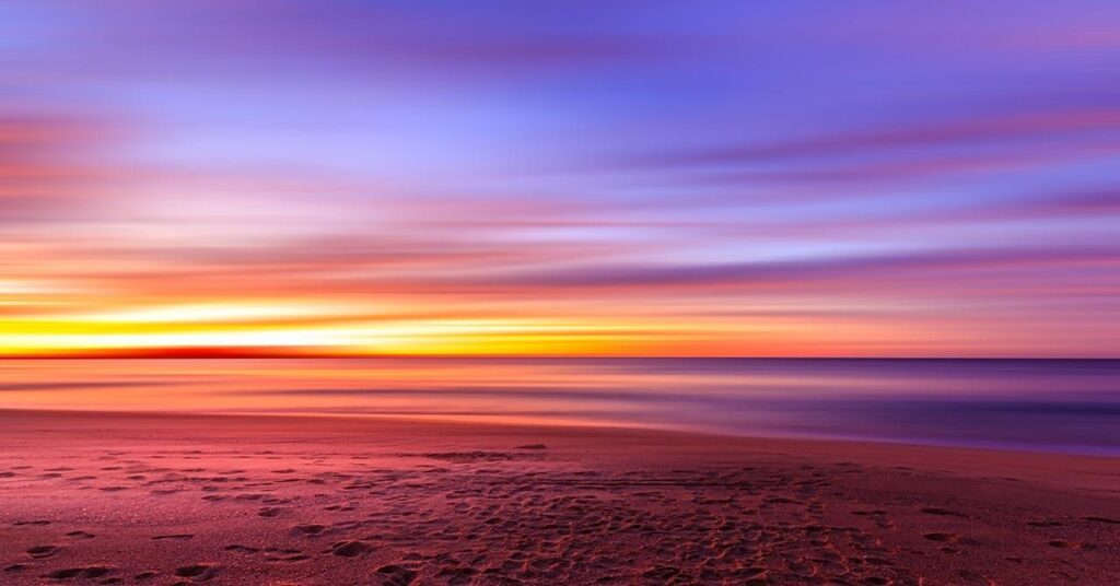 A golden sun rises on the horizon of a beach