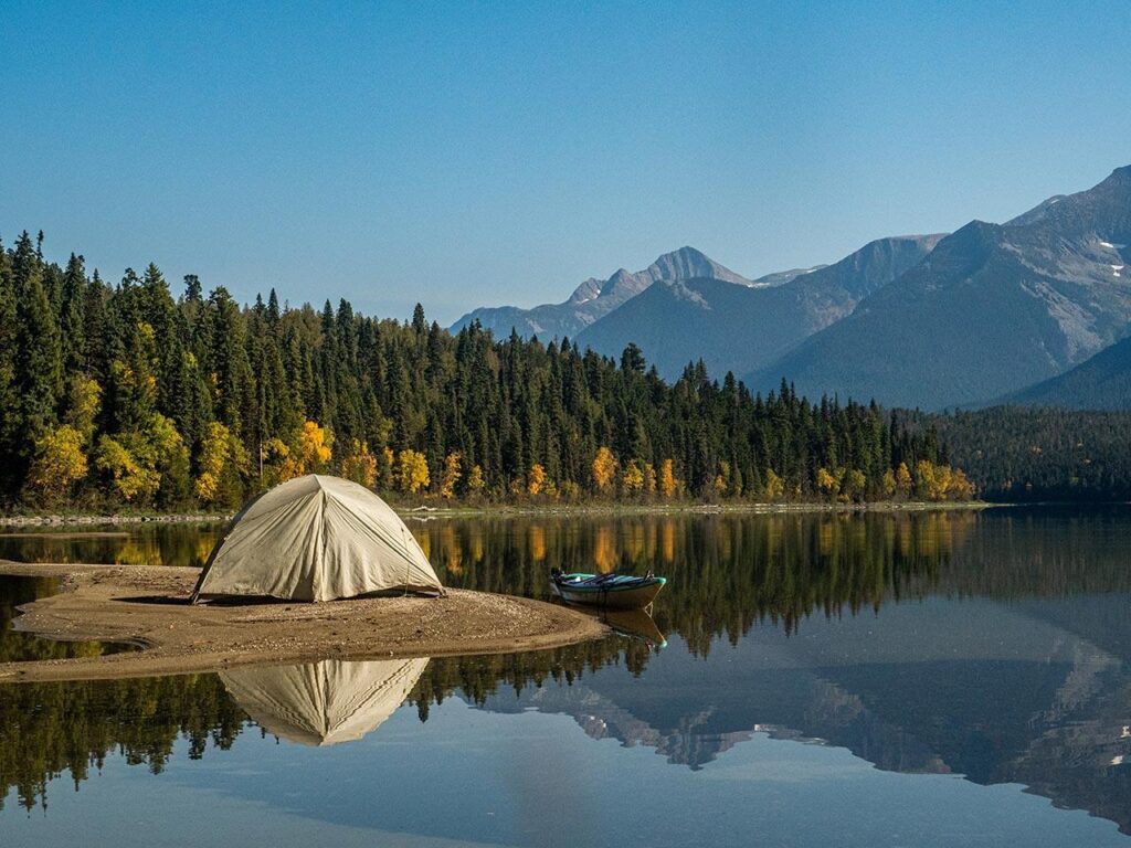A tent sits in front of a lake, a mountain, and some trees